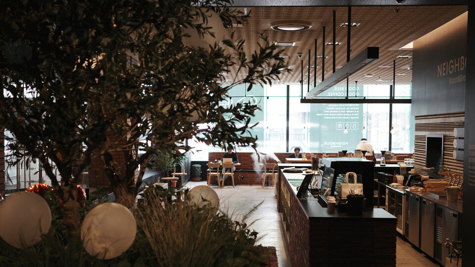 A light-filled coffee house with communal tables where people work on laptops